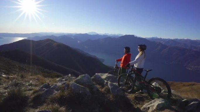 男人和女人坐在山顶上的山地自行车上，看着远处