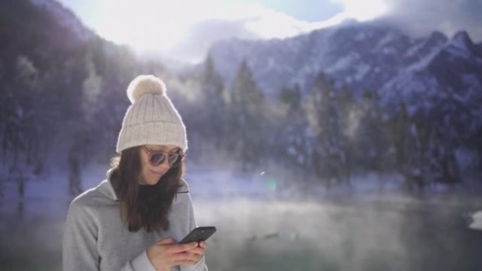 年轻女子在白雪皑皑的湖边用手机发短信