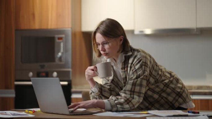 一个女人喝咖啡，看着笔记本电脑看文件
