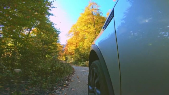 在阳光明媚的秋天森林中的碎石路上行驶的汽车的LD前轮胎