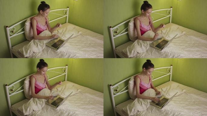 一名年轻女子晚上躺在床上，用笔记本电脑和信用卡在互联网上购物。