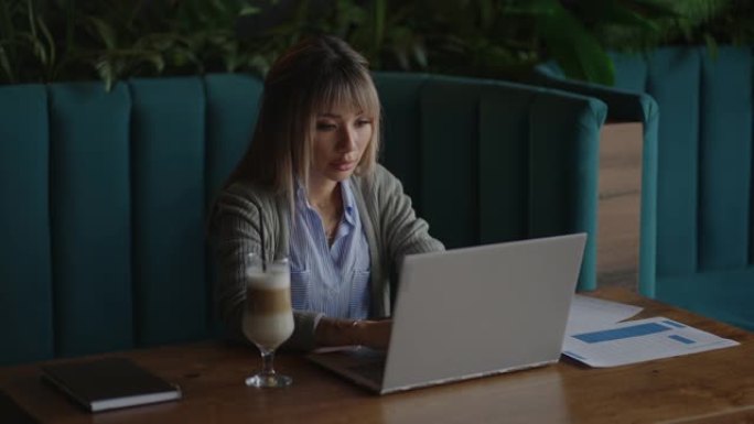 年轻的亚洲漂亮的女办公室职员坐在笔记本电脑在桌子上，工作和思考。