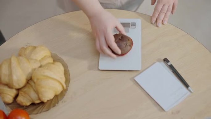 女人将松饼放在厨房秤上，计算卡路里，碳水化合物的摄入量