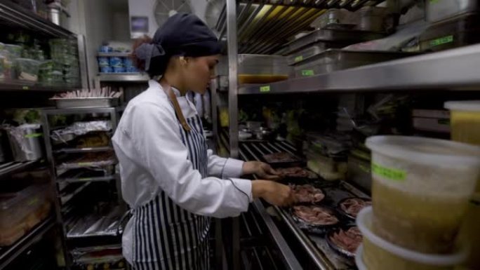 女烹饪助理在餐厅的冷藏室里用火腿组织一些菜肴