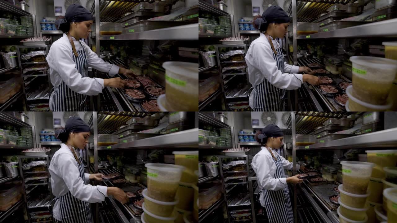 女烹饪助理在餐厅的冷藏室里用火腿组织一些菜肴