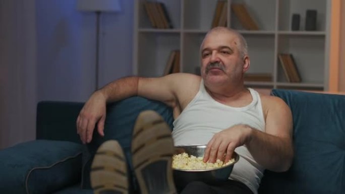 该男子坐在沙发上，用左手吃爆米花。近距离拍摄