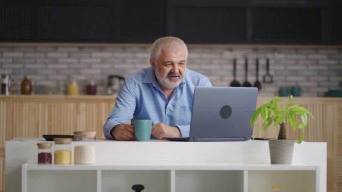 老人正在与朋友或家人通过笔记本电脑进行视频通话，在家庭厨房里的人的肖像