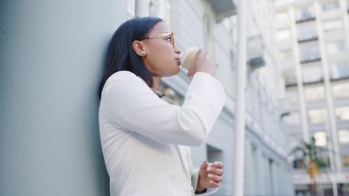 年轻的女商人喝咖啡靠在城市的建筑物上。公司专业人士在休息时看起来很体贴。自信的高管在镇上享受外卖茶