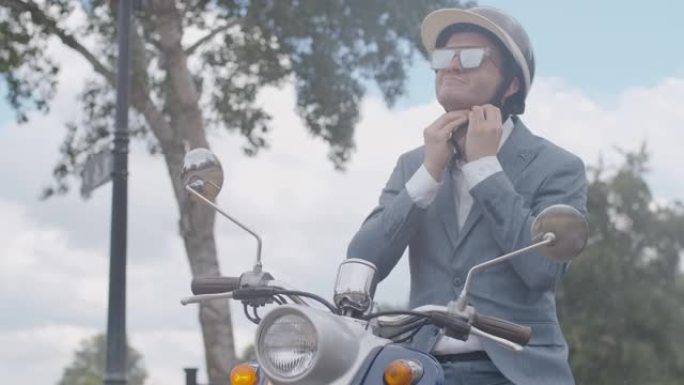 坐在户外摩托车上时，积极自信的男人在慢速戴上头盔的中间镜头。微笑的男性高加索骑自行车的人在下雨的夏天