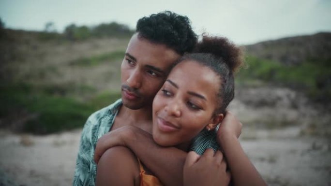 热爱非洲种族的夫妇坐在沙滩上，互相抱着。海边的浪漫约会