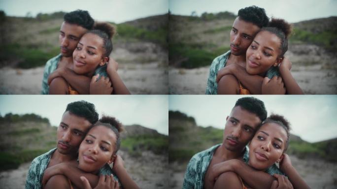 热爱非洲种族的夫妇坐在沙滩上，互相抱着。海边的浪漫约会