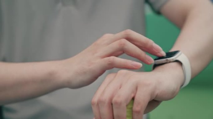 年轻的亚洲男子在开始网球比赛前安装智能手表来衡量自己的健康状况。