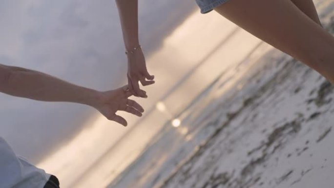 手牵手的夫妇。日落海滩上紫色和橙色天空的轮廓。特写