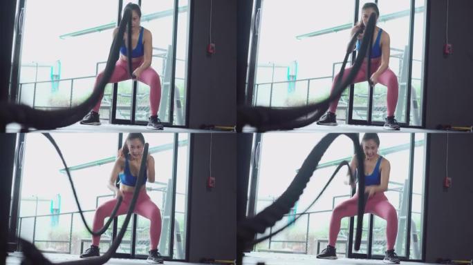 强有力的、有吸引力的、肌肉强健的女性健身教练在健身房用绳子做战斗训练。