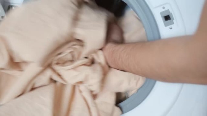 男人的手在洗衣机上装米色床单，在家洗衣服。