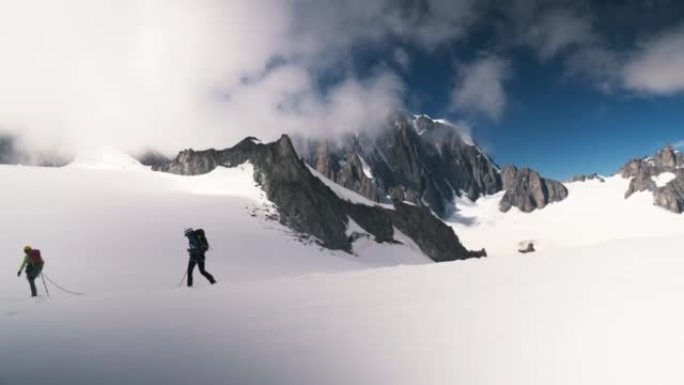 一队登山者沿着欧洲阿尔卑斯山的冰盖斜坡移动。遥远的轮廓