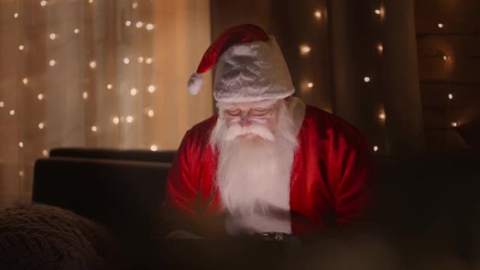 圣诞老人在圣诞灯火下晚上用笔记本电脑工作的肖像