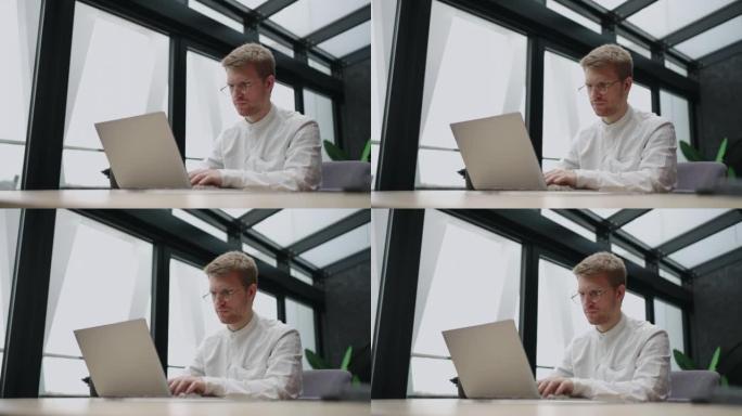 帅哥白天在现代办公室用笔记本电脑工作，穿着白衬衫的人在网上冲浪