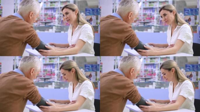支持高级男子说话的积极女性肖像在药房用血压计测量血压。美丽的高加索药剂师在药店帮助不适的客户。