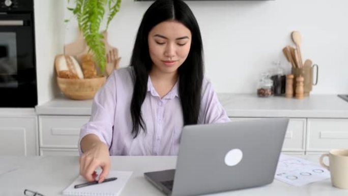远程学习，在线课程。专注的聪明的中国女学生，穿着时尚的休闲服，远程学习，使用笔记本电脑，在在线演讲中