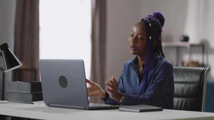 年轻的黑人妇女正在通过笔记本电脑上的视频聊天进行交流，与家庭办公室的客户或同事聊天