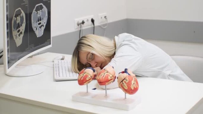 兽医精疲力尽，在电脑屏幕附近的桌子旁睡着了。一位女医生在工作场所打瞌睡，在一次大手术后筋疲力尽，非常