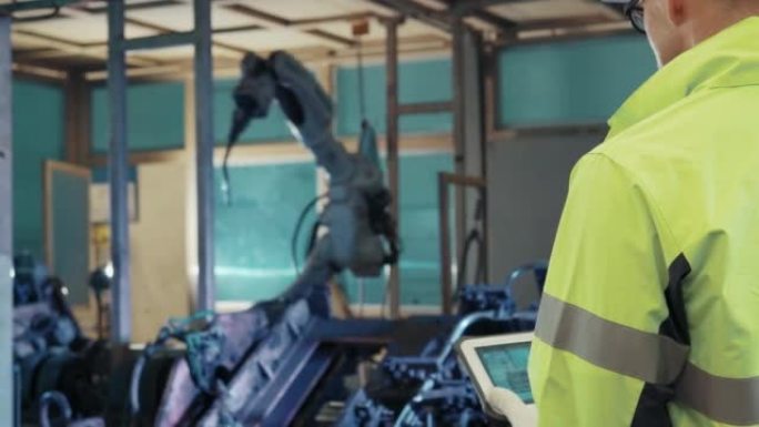 保护工作服的技术工程师在工厂中控制和指导在工业机器人上工作的机械臂的维护