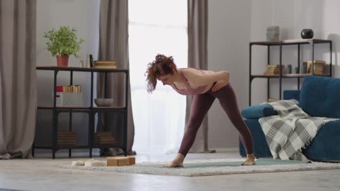 年轻苗条女人在家瑜伽锻炼，女士站在客厅训练，做静态体式