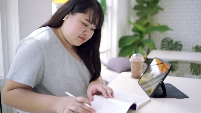 大型女性在咖啡店在线学习并在平板电脑上做笔记。