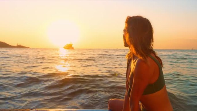 SLO MO女人坐在海上的桨板上看日落