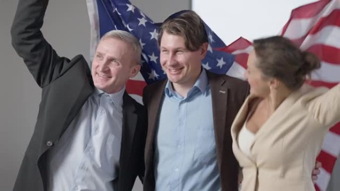 一群带着美国国旗的快乐商人面带微笑。激动的成功男人和女人在室内办公室为创业成功感到高兴。民族爱国主义