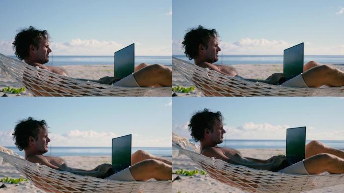 男子用笔记本电脑躺在海滩上两棵棕榈树之间的吊床上