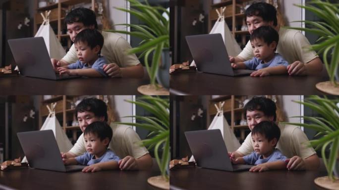 父亲抱着儿子在家时使用笔记本电脑