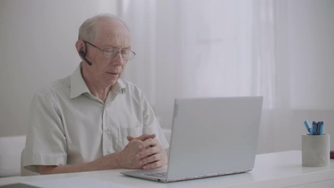 老人正在使用笔记本上的视频通话，坐在家里，与同事交流，自我隔离和远程工作