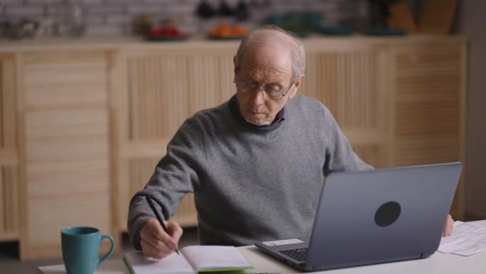 老人正在计算自己的费用和计划预算，坐在家里，用计算器计数并在笔记本电脑上打字