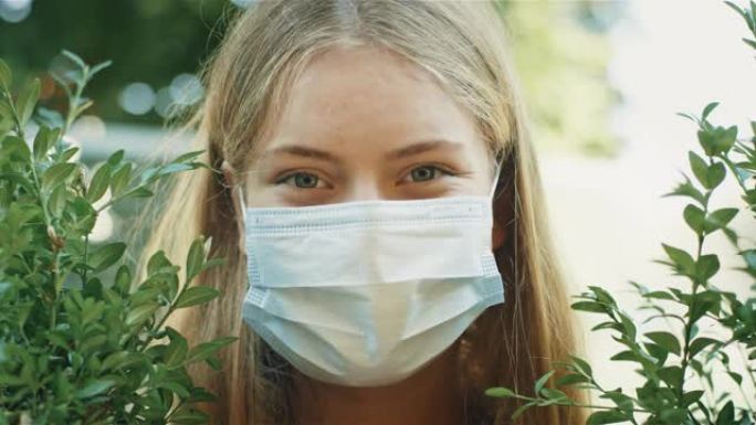 微笑的年轻女子戴着面膜保护病毒。在树篱中