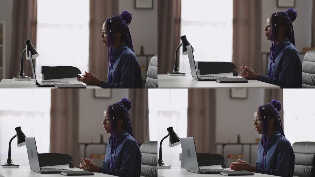 黑人妇女正在网上咨询，坐在笔记本电脑旁，看着网络摄像头并回答问题