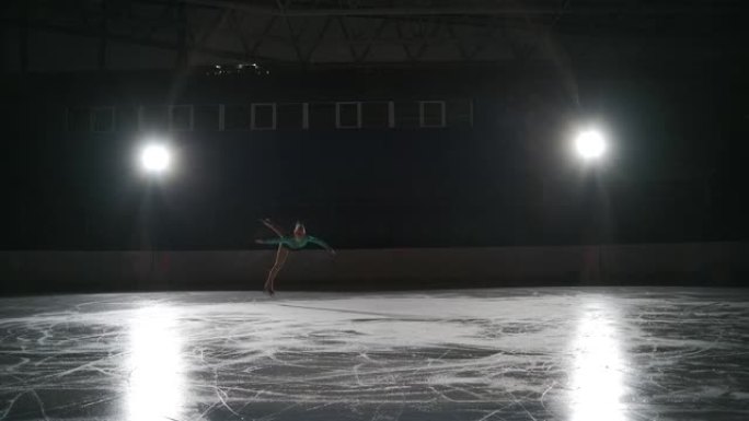 少年单身女子花样滑冰运动员独自在黑暗的空旷体育场上训练，女孩独自在溜冰场上滑冰