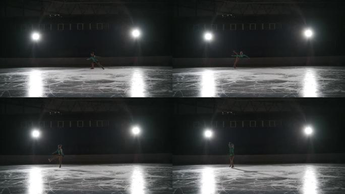 少年单身女子花样滑冰运动员独自在黑暗的空旷体育场上训练，女孩独自在溜冰场上滑冰
