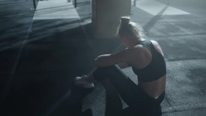 疲惫的女运动员在健身房辛苦训练后哭泣，独自坐在地板上，遭受身体的疼痛