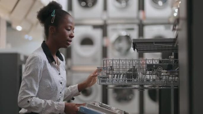 快乐的年轻黑人妇女正在家电商店看洗碗机，购买厨房设备