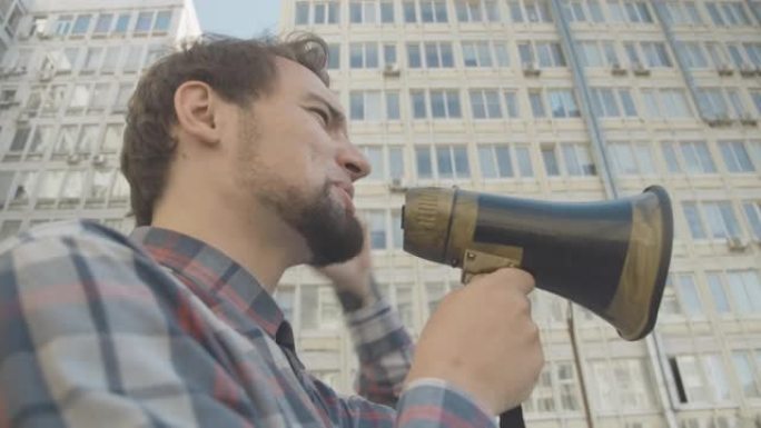 侧面的特写愤怒的人大喊通过扩音器和手势。白人抗议者在城市鼓励示威游行的肖像。为人权而暴动。电影4k 