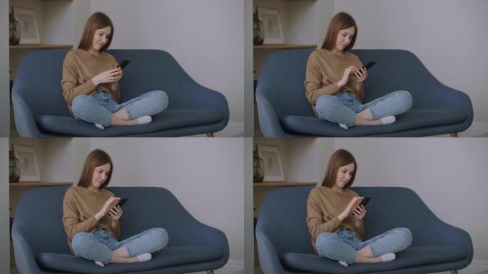 女商人在家庭办公室用手机打字信息。年轻女孩在电话里慢动作聊天。在沙发上使用智能手机关闭年轻女性的手。