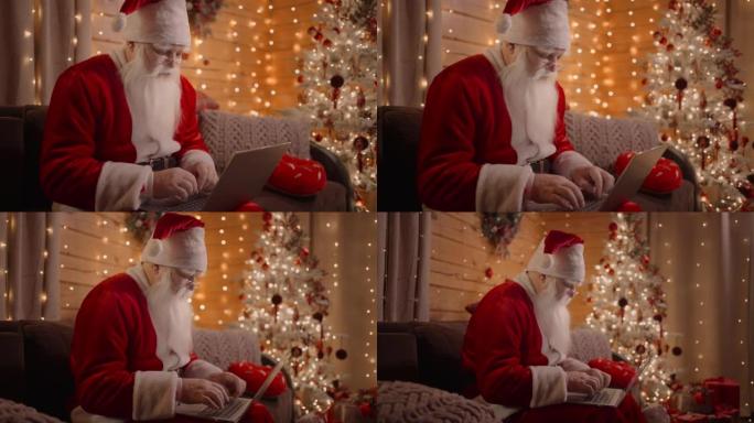 圣诞夜，一个真正的圣诞老人在笔记本电脑上行走在家里的沙发上的肖像。圣诞老人回复电子邮件，浏览互联网银