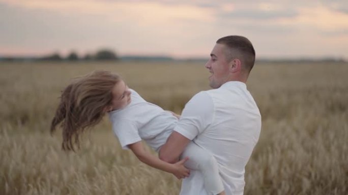 一位父亲在日落时拥抱并环绕着他心爱的女儿。在女孩的田野中日落时盘旋的慢动作