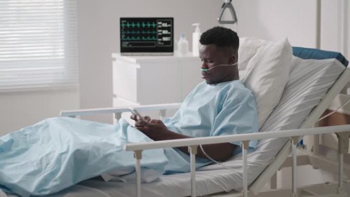 一名黑人男子躺在医院的病床上，从医院向他的朋友和亲戚提供信息。通过互联网和移动设备与医院中的亲人交流