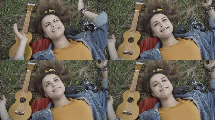 迷人的无忧无虑的高加索嬉皮士女人躺在草地上，睁开眼睛，对着镜头微笑。快乐美丽的女士在20世纪60年代