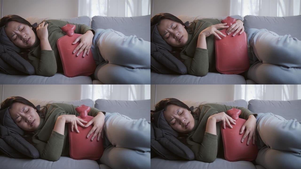 月经来潮严重的病女正在肚子上敷热水袋，缓解疼痛，在客厅沙发上感觉更好