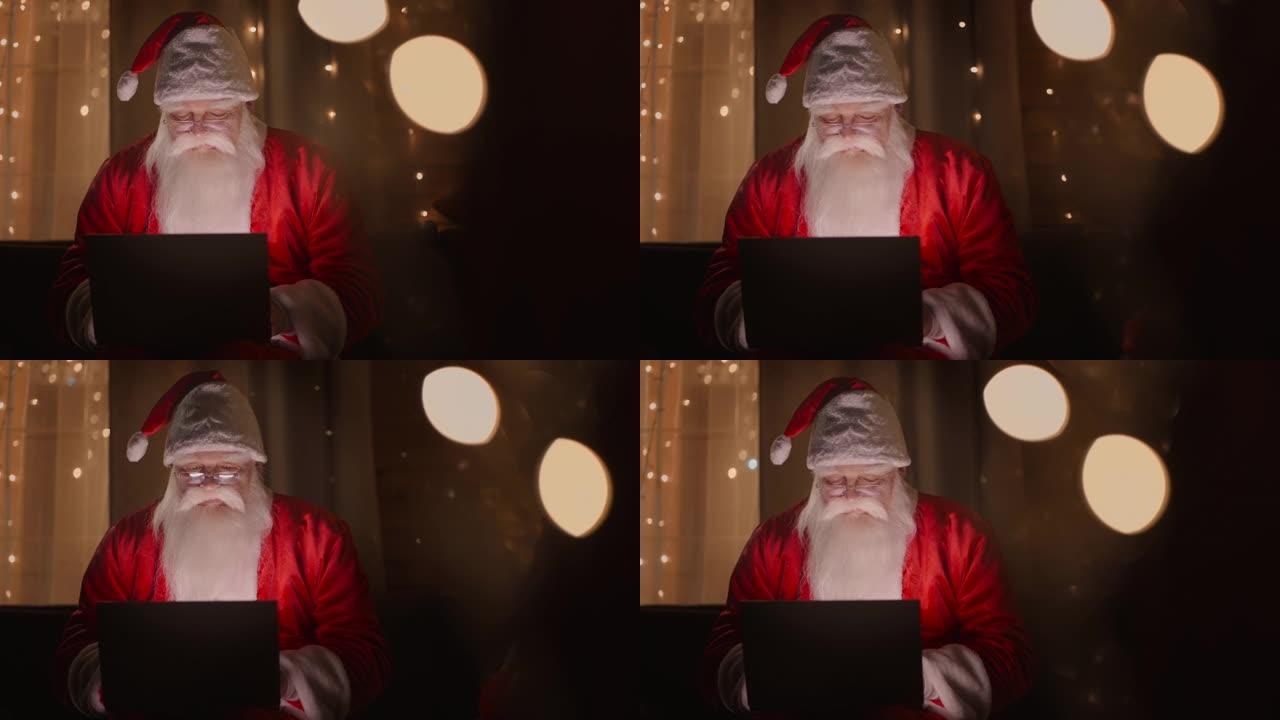 圣诞老人在圣诞节的灯光下在晚上用笔记本电脑工作