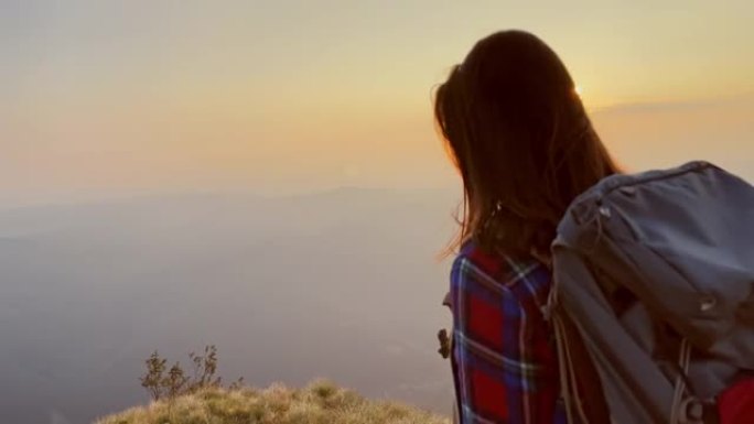 TS女徒步旅行者到达山脊的边缘，向日落举起双手